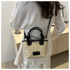 Detail of minimalist straw bucket bag with black leather straps on a side model view