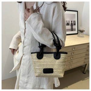 Detail of woven straw tote bag featuring black leather handles and knotted strap accents