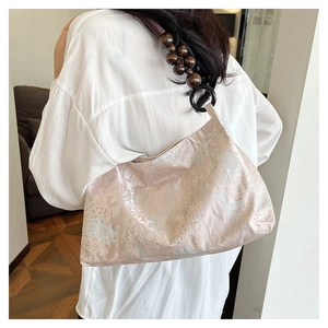 Detail of champagne satin shoulder bag featuring traditional patterns and wooden bead strap