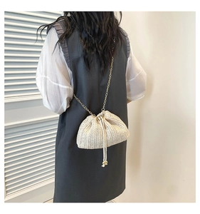 Detail of woven straw crossbody bag with golden chain strap and drawstring on model