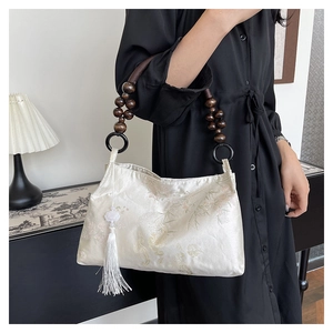 Close-up of white satin handbag featuring bamboo embroidery and wooden bead handle with tassel