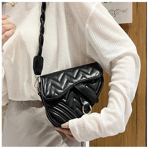 Close-up of black quilted saddle bag with golden hardware and woven shoulder strap