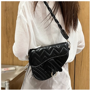 Detailed view of black saddle bag with V-shaped stitching and woven shoulder strap