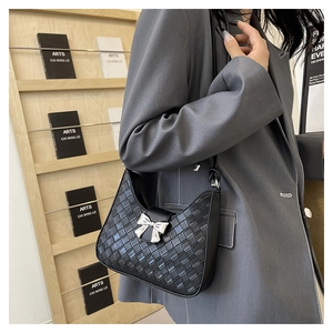 Detail of black woven leather hobo bag with a metallic silver bow clasp on the shoulder