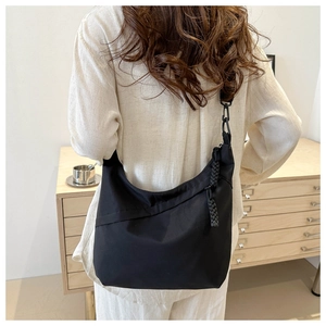 Close-up of a crescent black tote bag with woven zipper detail and wide shoulder strap