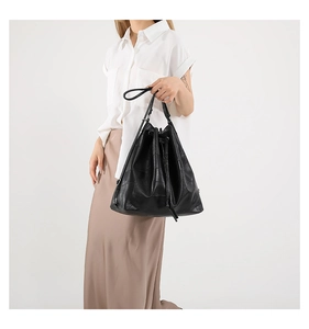 Detail of black embossed leather drawstring bucket bag on a model in a minimal setting