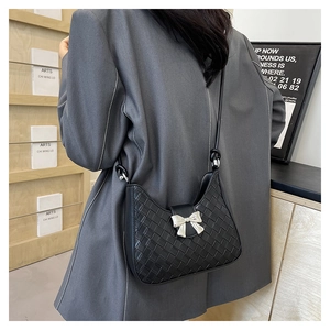 Detail of black woven shoulder bag featuring a silver metal bow accent and vintage texture