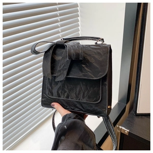 Close-up of black bow backpack with unique wrinkled texture and elegant hand-held strap