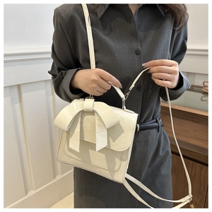 Detail of cream white bow crossbody bag with textured faux leather and top handle design