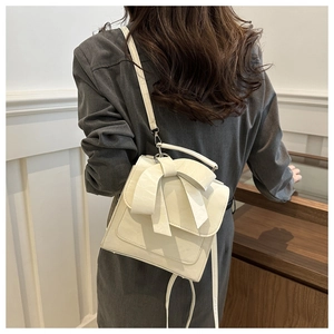 Detailed back view of a cream bow-accented multi-way backpack on a model