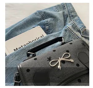 Detail of grey herringbone fabric handbag featuring black polka dots and silver metal bow