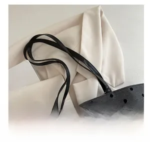 Detail of black polka dot tote bag featuring a silver bow charm and woven texture