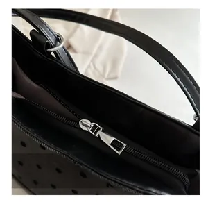 Detail of silver metal zipper and laser-cut perforated texture on a black tote bag