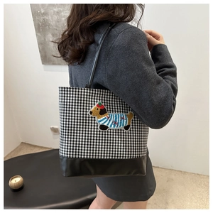 Detail of checkered tote bag featuring a cute plush puppy patch and leather bottom trim