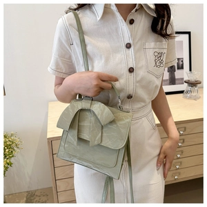 Detail showing the large decorative bow and textured PU leather of the light green handbag