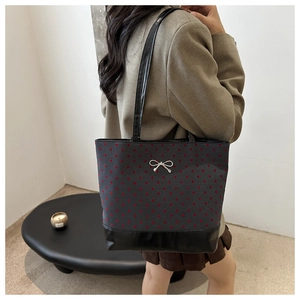 Detail of grey polka dot tote bag with silver metal bow worn by model in minimalist setting