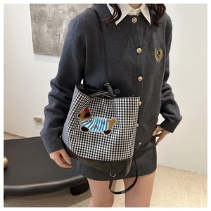 Detail of checkered bucket bag featuring dog embroidery and premium leather trim