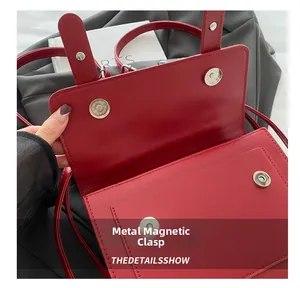 Detailed view of silver magnetic snap closures on a red leather messenger flap bag