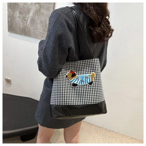 Detail of plaid tote bag with dachshund embroidery and leather straps on model