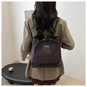 Rear view of a model wearing the dark grey polka dot backpack with a silver bow detail