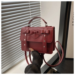Detail of burgundy leather satchel with decorative bows and silver metallic heart studs