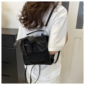 Detail of black bow backpack featuring pleated faux leather texture and slender straps