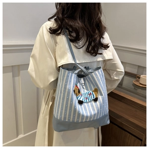 Detail of blue striped canvas tote bag with cartoon dog patch and leather bottom panel