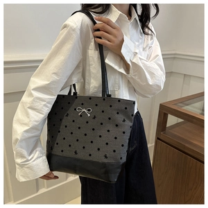 Close-up of gray polka dot tote bag with metal bow detail and black leather base