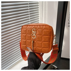 Detail of bright orange quilted crossbody bag with gold S-buckle and tassel accent