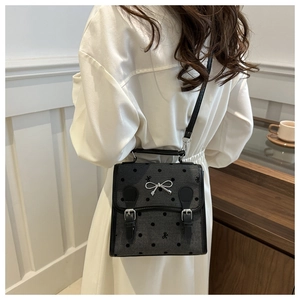 Detail view of a grey polka dot canvas crossbody bag with silver bow and leather straps
