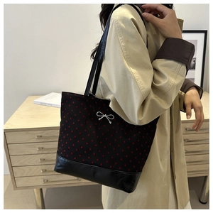 Black canvas tote bag with red heart pattern and silver bow detail on model in warm setting