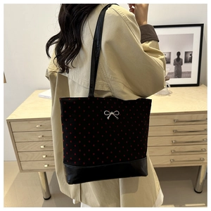 Detail of black tote bag featuring red heart patterns and a silver bow on leather base