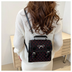 Detail of a black mini backpack with red heart prints and a silver bow buckle decoration
