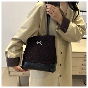 Detail of black heart print tote bag with silver bow and leather base worn with trench coat