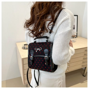 Detail of a black heart-print backpack worn over a white sweater in a cozy setting