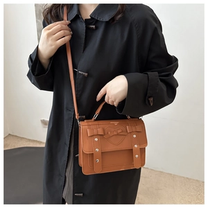 Brown vintage satchel bag with heart patch, bow detail, and silver rivets on a black coat