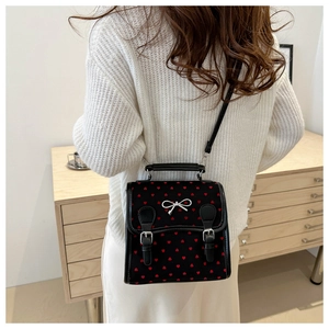 Detailed view of black crossbody bag with red heart pattern and silver bow on model