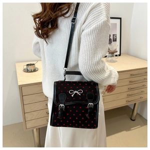 Detail of black crossbody bag with red heart patterns and silver bow on its cover