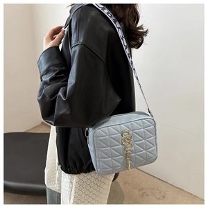 Close-up of light blue quilted crossbody bag with golden S-logo and tassel detail