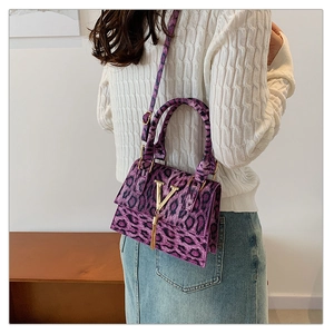 Dettaglio della borsa a tracolla leopardata viola con logo V dorato e nappina indossata