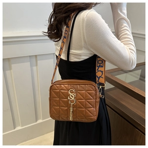 Close-up of brown quilted shoulder bag with golden S charm and ethnic woven strap