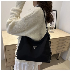 Detail of black nylon shoulder bag with silver chain strap and metal logo on a model