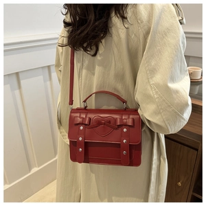 Model wearing retro red crossbody bag with heart and bow details over a beige trench coat