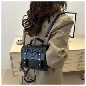 Detail of black PU leather shoulder bag with embossed heart and bow detail on a model