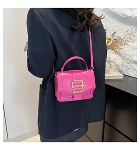 Detail of a bright fuchsia crossbody bag with gold metal buckle and top handle