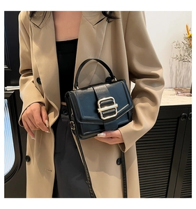 Close-up of minimalist black rectangle handbag with gold buckle and stylish beige coat