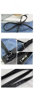 Detail view of blue denim tote bag with black leather trim and silver metal zipper