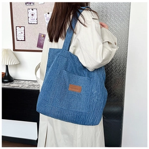 Detail view of a blue corduroy tote bag featuring a leather patch and side pocket