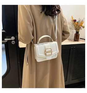 Detailed view of white leather crossbody bag with gold buckle on a beige trench coat