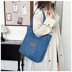 Close-up of blue canvas tote bag with a leather patch shown on model's shoulder